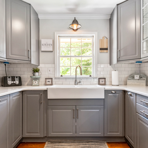 Trendy kitchen interior of one of our vacation rentals. Gray drawers with white granite countertops and daylight coming through a front window.